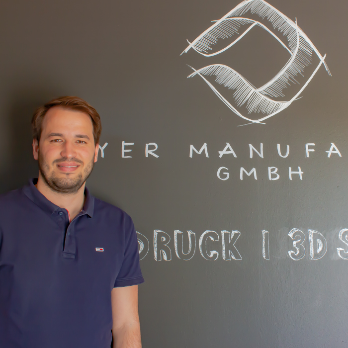 Tim Riedmüller vor dem Logo seines Unternehmens